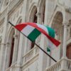 Bandera de Hungría ondeando frente a la fachada del Parlamento en Budapest, con su arquitectura neogótica característica.