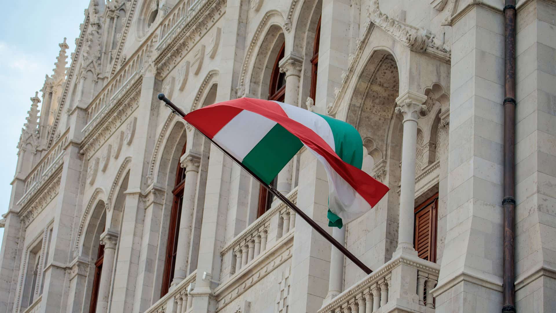 Bandera de Hungría ondeando frente a la fachada del Parlamento en Budapest, con su arquitectura neogótica característica.