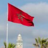 Bandera nacional de Marruecos ondeando frente al minarete de la mezquita Hassan II en Casablanca, Marruecos en un cielo claro y despejado.