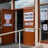 Entrance to a polling station in the Kingston upon Hull East constituency during the 2024 United Kingdom general election. Open wooden doors display large “Polling Station” and “Way In” signs, while an accessible ramp with white handrails leads to the entrance. Notices and election information are posted on the windows and doors, and reflections of the street and parked cars can be seen in the glass.