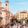 Vista panorámica de la Puerta del Sol de Madrid con la Real Casa de Correos, edificios históricos y peatones caminando por la plaza.