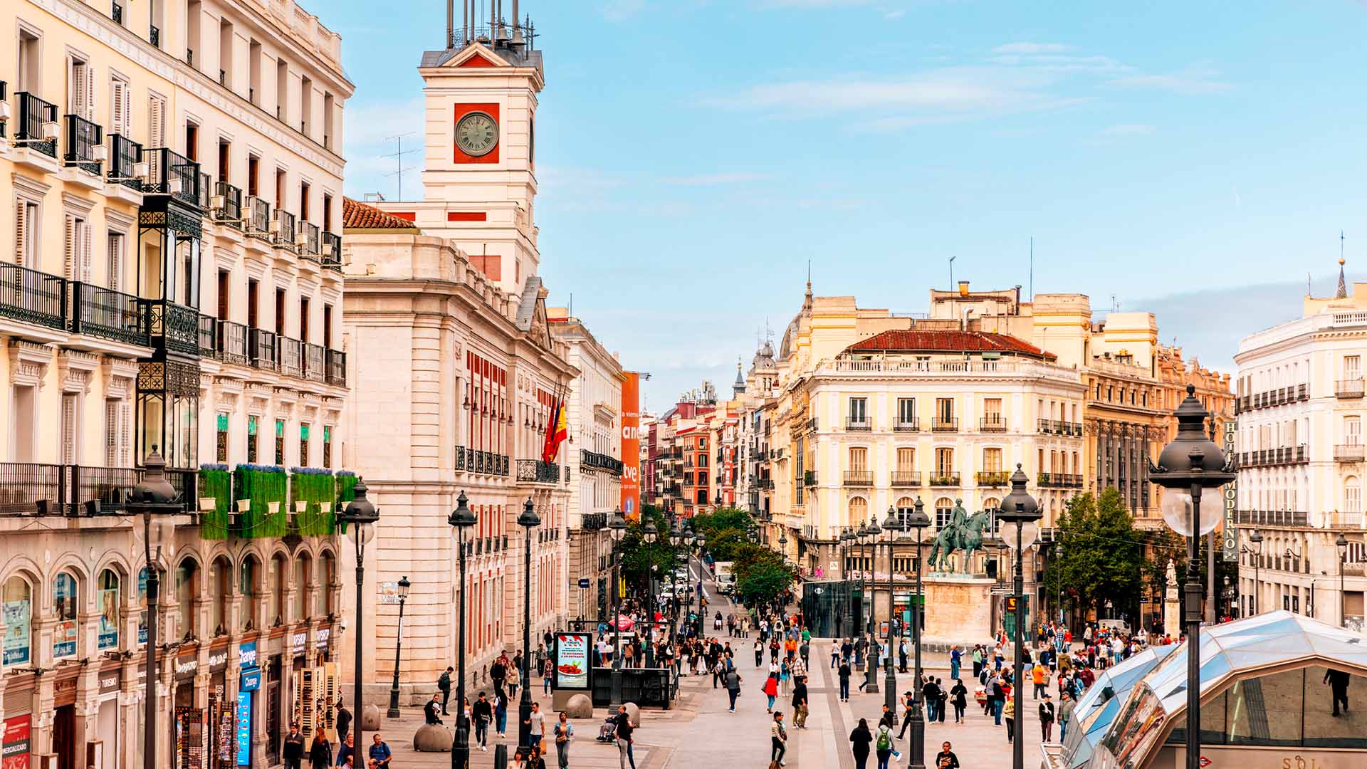 Vista panorámica de la Puerta del Sol de Madrid con la Real Casa de Correos, edificios históricos y peatones caminando por la plaza.