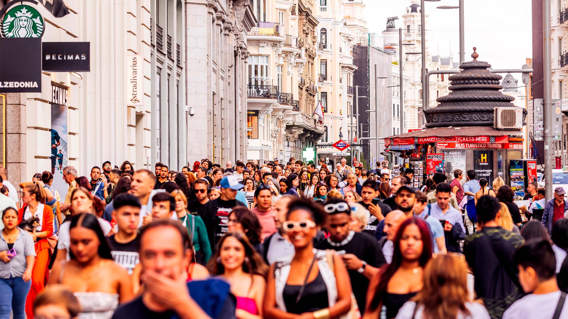 Gran Vía de Madrid llena de peatones junto a tiendas, cafeterías y edificios históricos en una concurrida tarde en el centro de la ciudad.