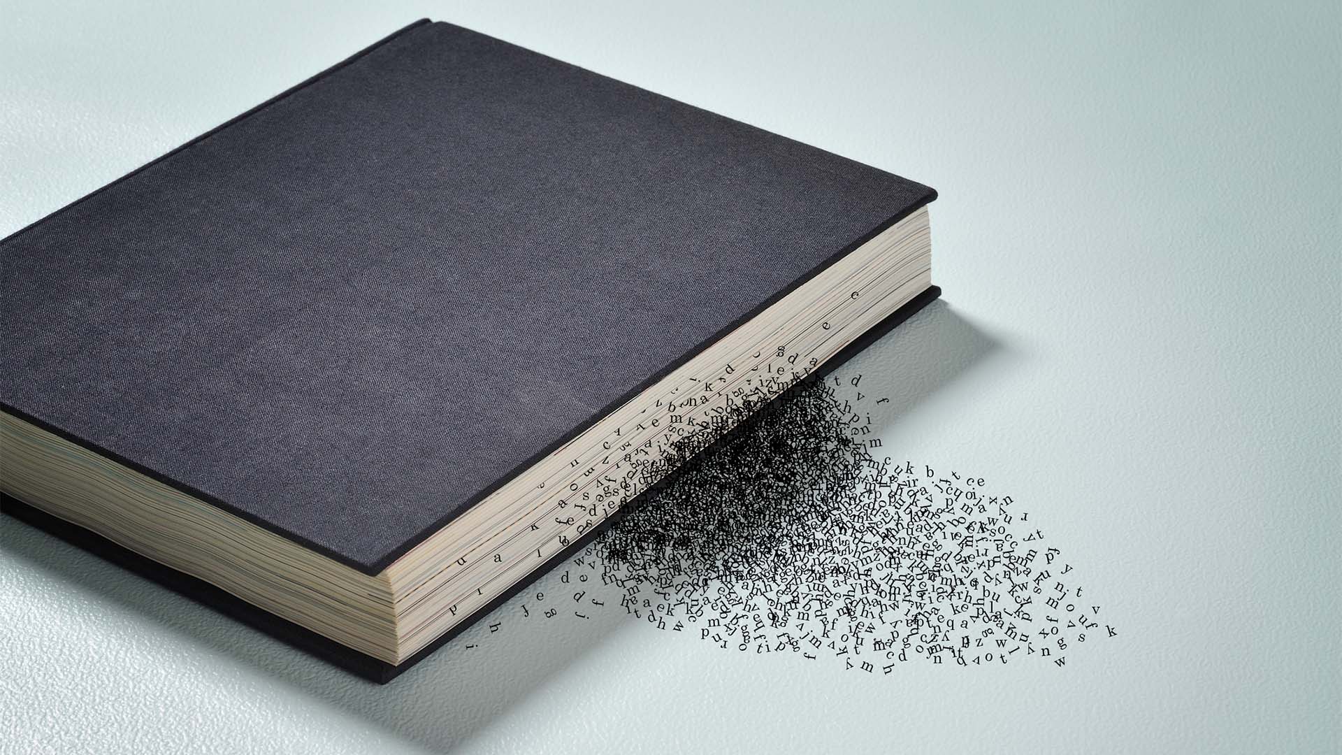 Closed black hardcover book on a light surface, with scattered letters emerging from the edge of the pages, creating the visual effect of words disintegrating.