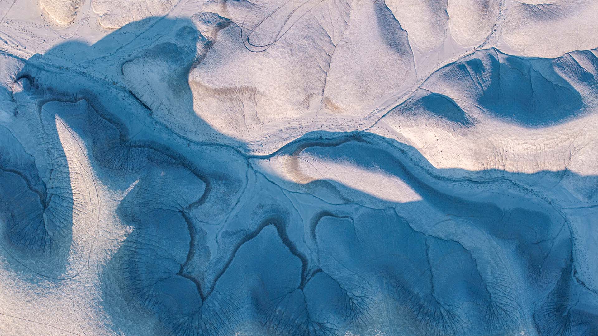 Vista aérea de un paisaje desértico en Utah donde la erosión ha modelado formas orgánicas y sinuosas. Las sombras azuladas recorren vaguadas y crestas claras, creando patrones abstractos.