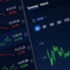 Primer plano de una pantalla de mercado financiero que muestra varios índices, cotizaciones y gráficos de evolución de precios. Se observan datos numéricos y variaciones porcentuales en rojo y verde sobre un fondo oscuro.