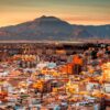 Panorámica de la ciudad de Alicante iluminada por la luz del atardecer, con edificios residenciales en primer plano y el monte Benacantil elevándose al fondo bajo un cielo despejado.