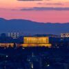 Vista panorámica de Ankara al atardecer con el mausoleo de Atatürk (Anıtkabir) iluminado en el centro de la ciudad. Al fondo se distinguen colinas, mezquitas y edificios bajo un cielo de tonos rosados y azulados.