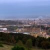 Panorámica de la refinería de petróleo de A Coruña al atardecer, con instalaciones industriales, depósitos de combustible y el entorno urbano y costero al fondo.