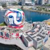 Vista aérea de Science World, en Vancouver, cubierto con una estructura que reproduce el diseño del balón oficial del Mundial de la FIFA 2026. El edificio se sitúa junto al puerto, rodeado de agua, embarcaciones y rascacielos de la ciudad.