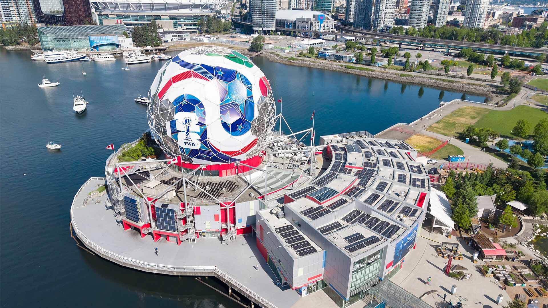 Vista aérea de Science World, en Vancouver, cubierto con una estructura que reproduce el diseño del balón oficial del Mundial de la FIFA 2026. El edificio se sitúa junto al puerto, rodeado de agua, embarcaciones y rascacielos de la ciudad.
