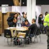 Interior de un centro de votación instalado en Corferias, Bogotá, con cabinas electorales, mesas de trabajo y personal realizando tareas de organización y recuento de votos, mientras un agente de la Policía Nacional supervisa la seguridad de la jornada electoral.