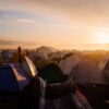 Campo de refugiados lleno de tiendas de campaña. En el horizonte, la vista del atardecer y un cielo nublado.