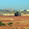 Vehículo blindado y varios soldados en una zona militar del aeropuerto internacional Diori Hamani, en Niamey, Níger, con hangares al fondo y terreno árido en primer plano. El cielo es claro aunque hay un ambiente empolvado.