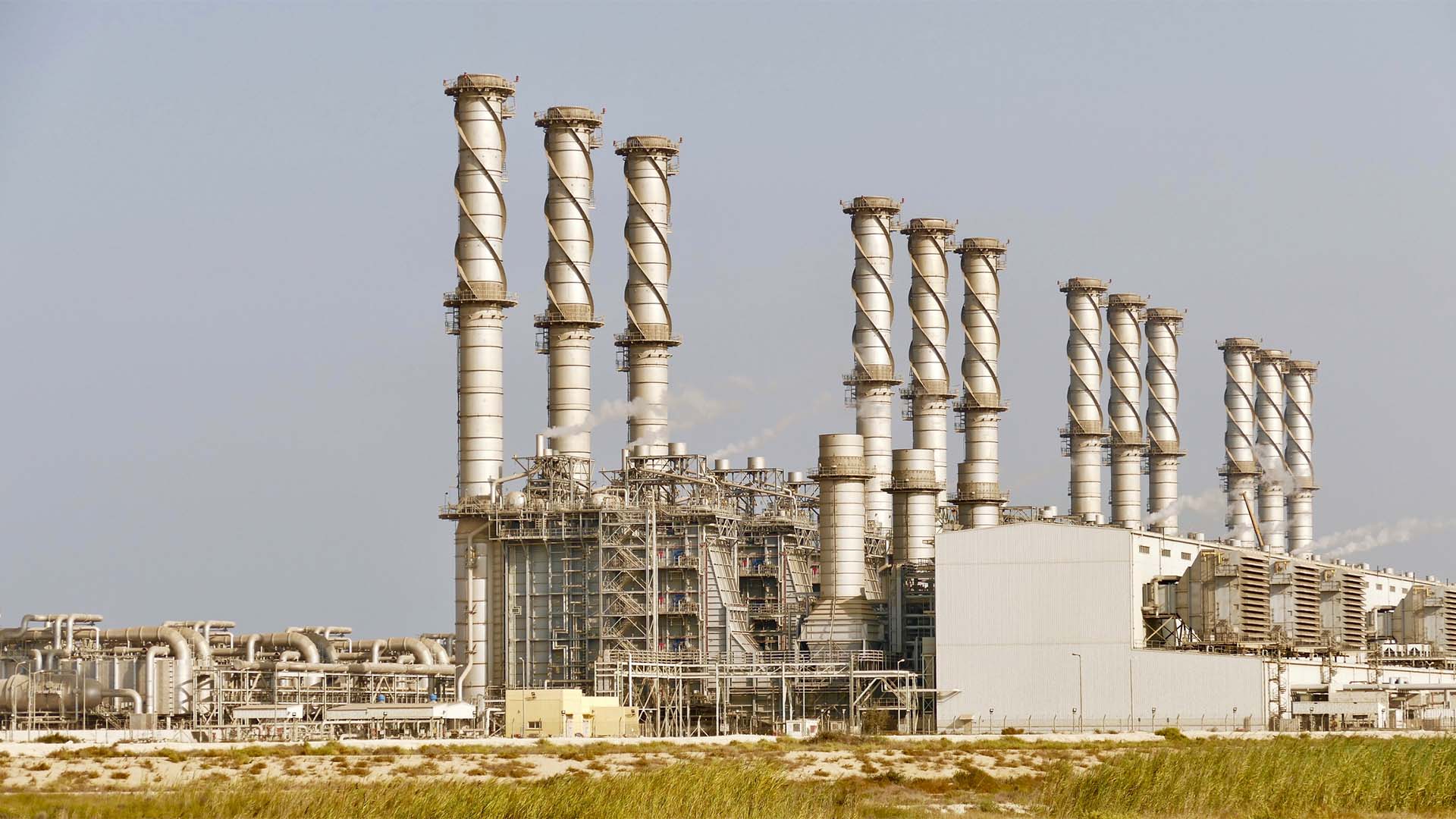Vista exterior de la planta desaladora de Jubail, con numerosos conductos, tuberías e instalaciones industriales y varias chimeneas altas de estructura helicoidal.