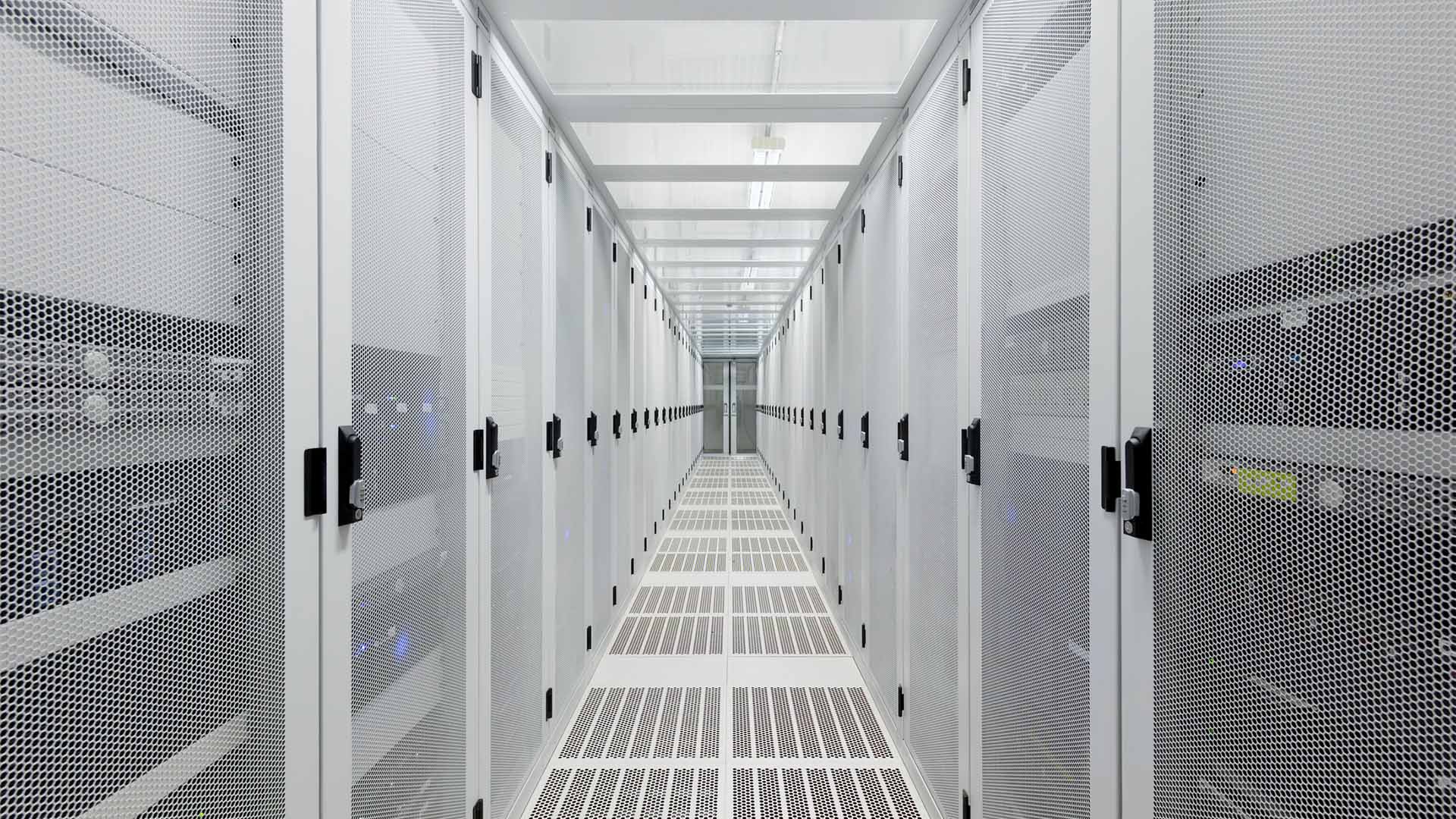 Pasillo de un centro de datos con largas filas de armarios metálicos blancos que albergan servidores y equipos de red.