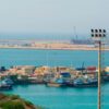Vista panorámica del puerto de Shahid Beheshti (Chabahar, Irán), con barcos pesqueros, contenedores, grúas e instalaciones portuarias junto al golfo de Omán, bajo un cielo despejado.
