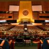 Vista panorámica del salón vacío de la Asamblea General de las Naciones Unidas, con filas de asientos y pupitres de los Estados miembros frente a la tribuna central y el emblema de la ONU.