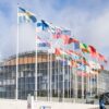 Exterior view of the European Investment Bank Group headquarters in Luxembourg’s Kirchberg district, with a row of European national flags in front of the curved glass-and-steel building.