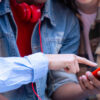 Tres adolescentes reunidos alrededor de un teléfono móvil rojo. Dos señalan la pantalla mientras uno de ellos (en el centro con camisa vaquera, camiseta y auriculares rojos al cuello) sostiene el dispositivo. La foto ilustra el acceso y la interacción con contenidos digitales y redes sociales de los adolescentes.