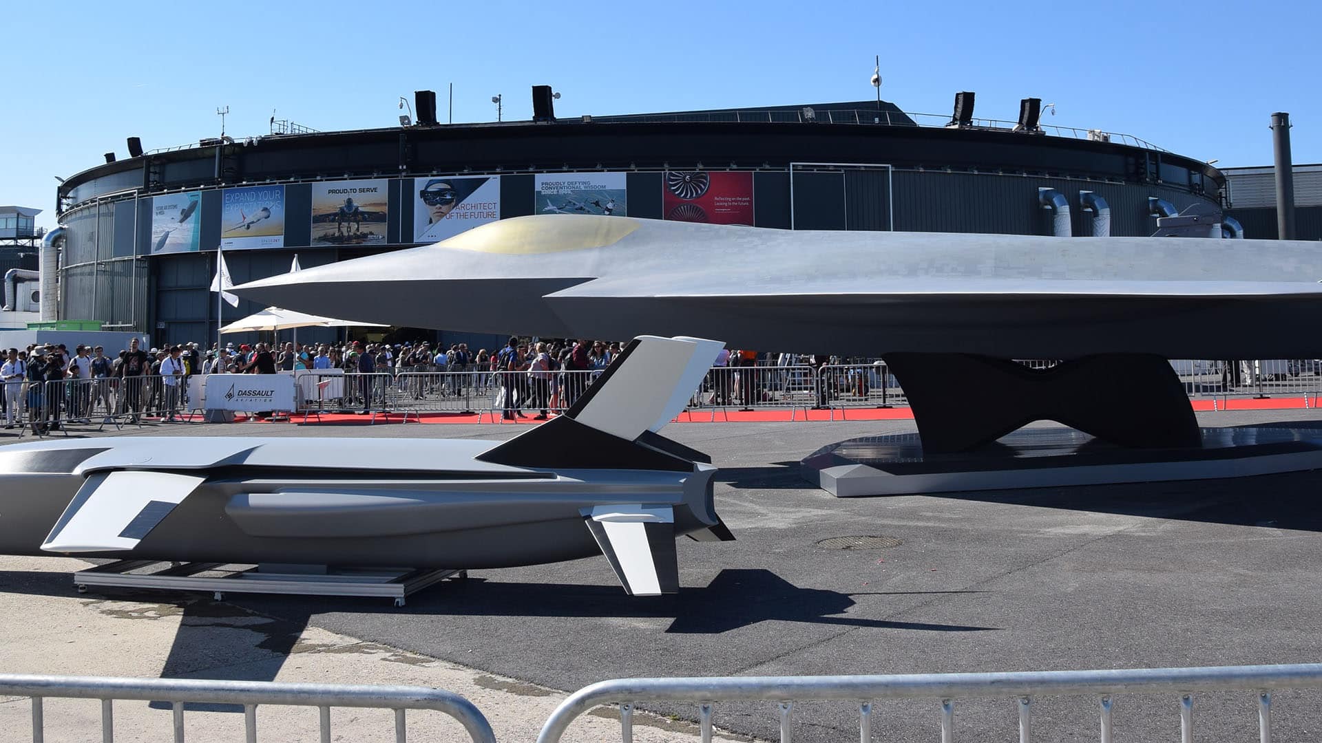 Exposición al aire libre de la maqueta a escala 1 del proyecto de avión de combate FCAS NGF (Next Generation Fighter) junto con los efectores externos expuestas en el stand de Dassault Aviation en el Salón Aeronáutico de Le Bourget 2019. Detrás de las barreras de seguridad, numerosos visitantes observan la muestra durante un evento del sector aeroespacial y de defensa bajo un cielo despejado.