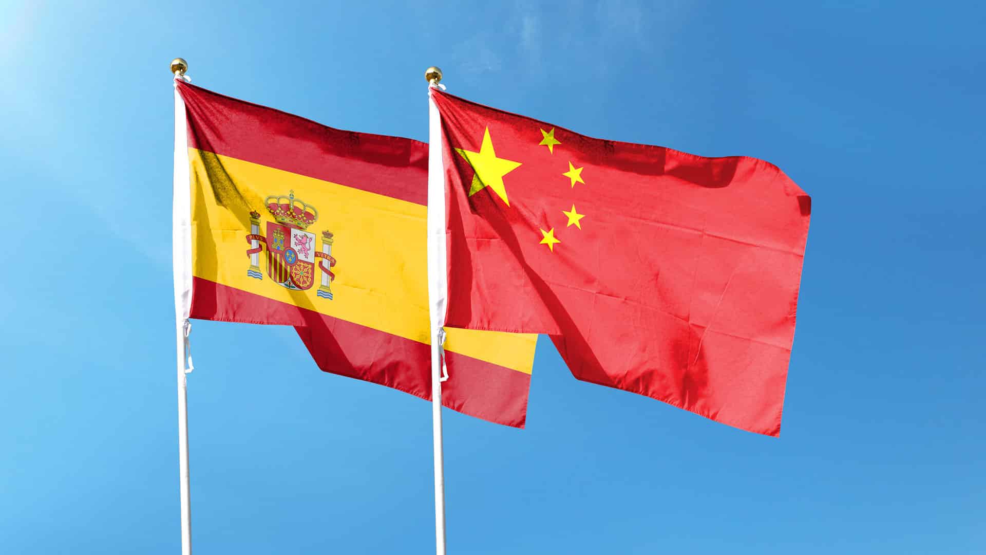 Banderas de España y de la República Popular China en sus respectivos mástiles ondeando en el cielo.
