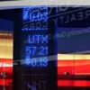 Pantallas electrónicas con cotizaciones bursátiles y datos financieros iluminados en azul, reflejadas sobre superficies acristaladas. Al fondo, logotipo del Bank of America y los espacios interiores de la sucursal bancaria.