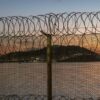 Vista de Ceuta desde Marruecos a través de la valla fronteriza con alambre de concertina, con el mar y la ciudad al fondo durante la puesta de sol.