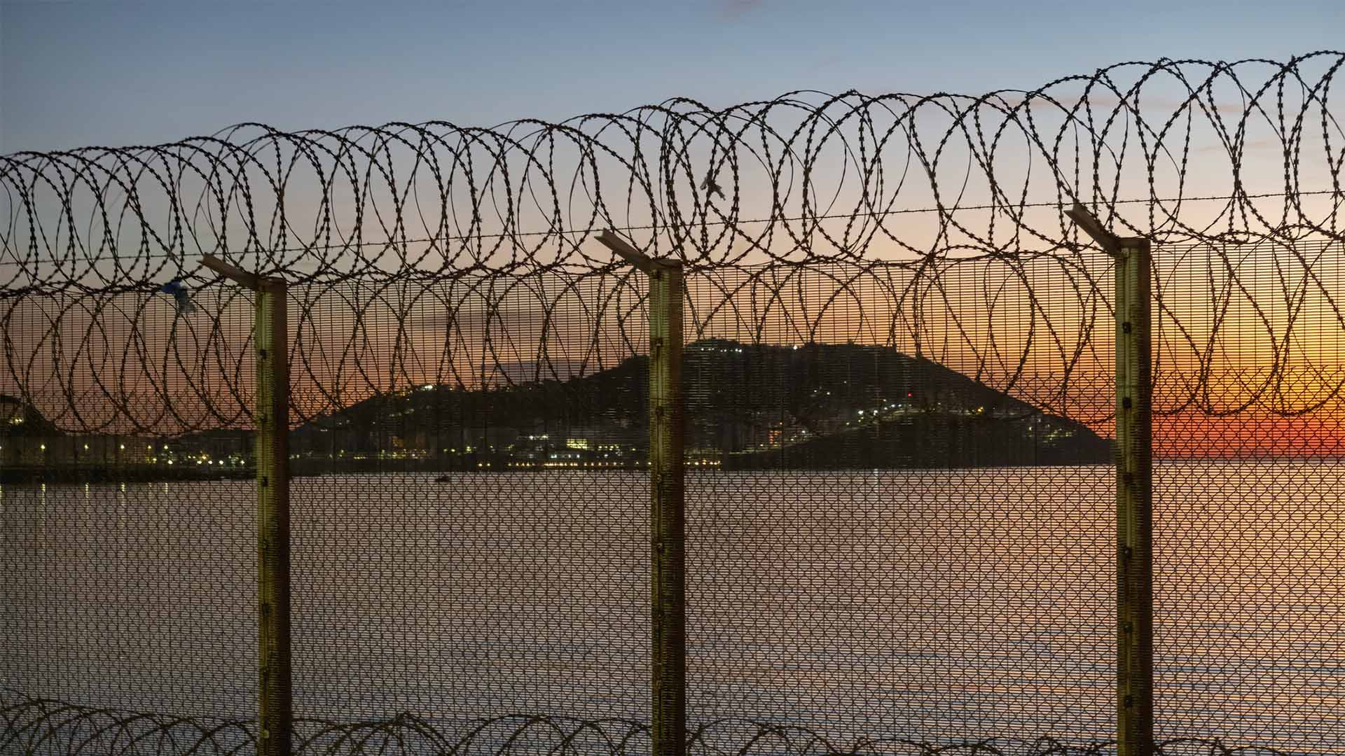 Vista de Ceuta desde Marruecos a través de la valla fronteriza con alambre de concertina, con el mar y la ciudad al fondo durante la puesta de sol.