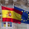 Banderas de España y de la Unión Europea ondeando juntas ante la fachada de un edificio institucional.