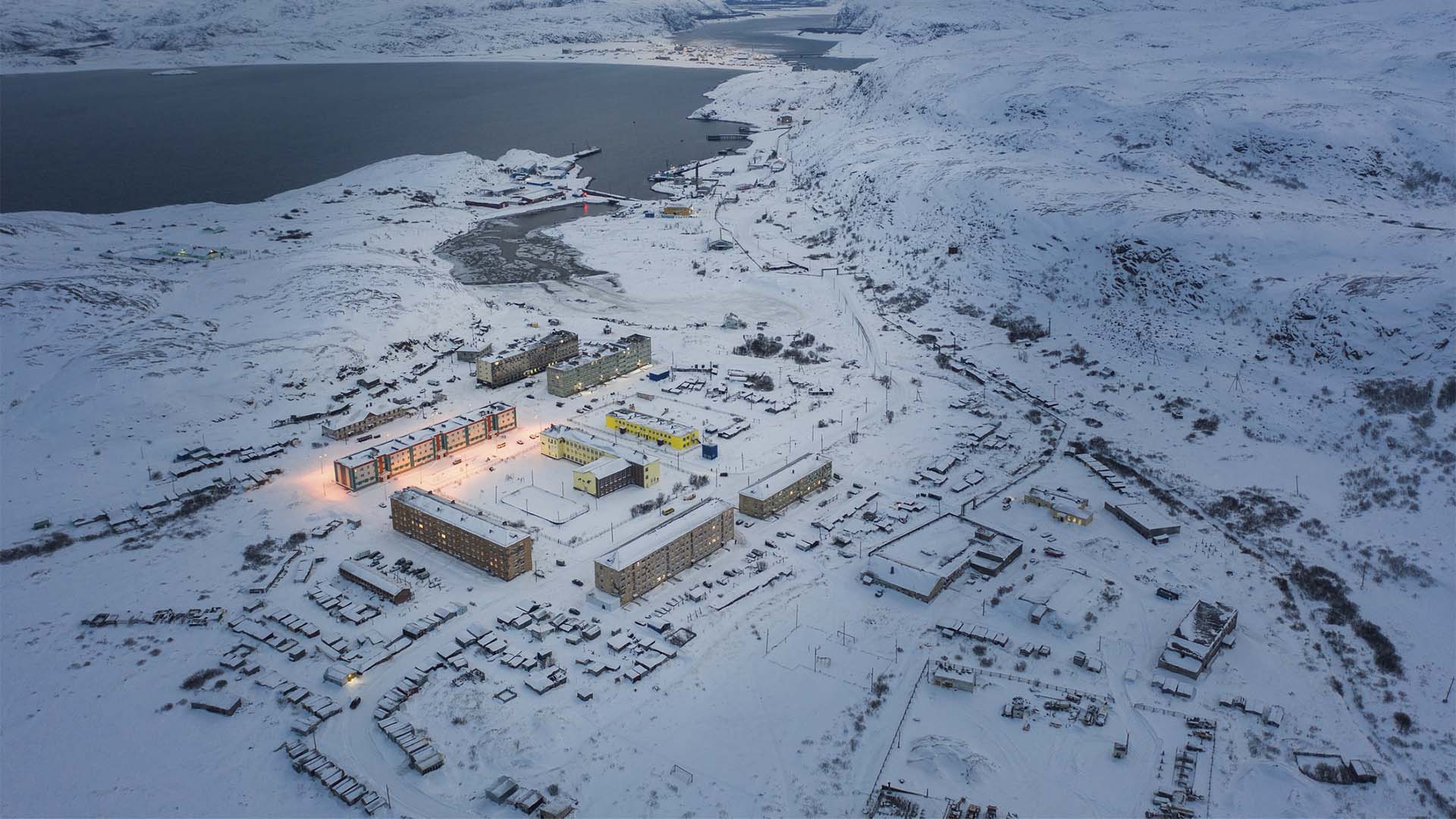 Vista aérea de Teriberka, en el Ártico ruso, con edificios junto a la costa rodeados por un extenso paisaje cubierto de nieve.