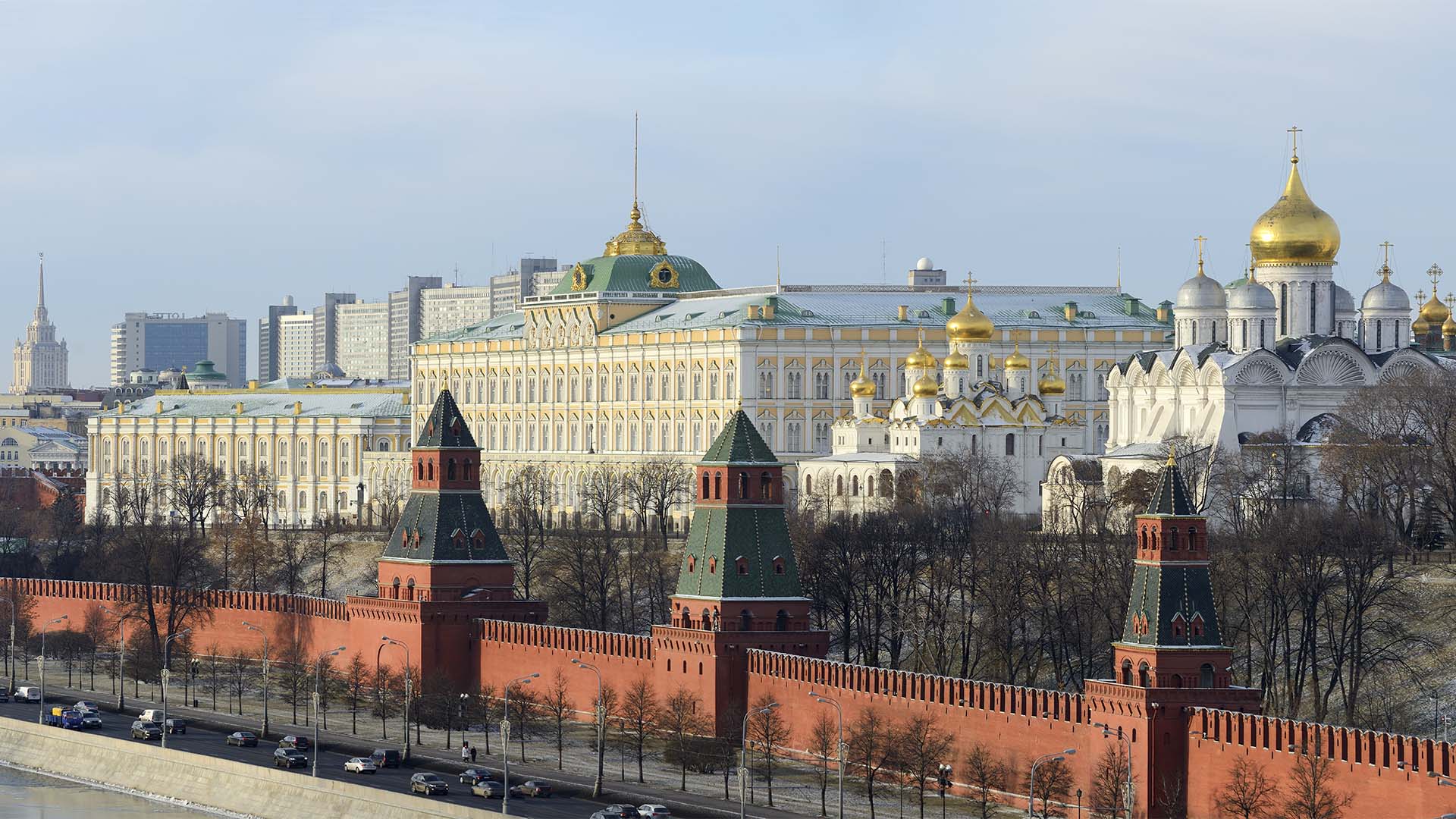 Vista panorámica del Kremlin de Moscú, con sus murallas y torres de ladrillo rojo en primer plano y el Gran Palacio del Kremlin y varias catedrales de cúpulas doradas al fondo.