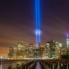 Horizonte urbano de Nueva York noche durante la instalación artística “Tribute in Light” en memoria de los atentados del 11-S, con dos haces de luz azul verticales proyectados al cielo desde los rascacielos junto al paseo marítimo.