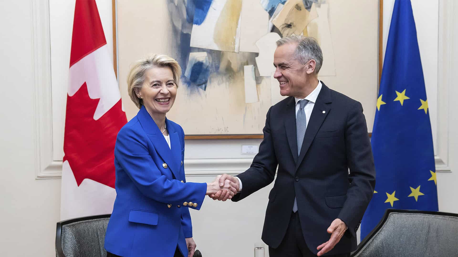 Ursula von der Leyen, presidenta de la Comisión Europea, y Mark Carney, primer ministro de Canadá, se estrechan la mano durante una reunión, con las banderas de Canadá y la Unión Europea al fondo.