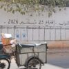 Un ciclomotor con un pequeño remolque pasa frente a unos paneles pintados en un muro sobre las elecciones legislativas en Marruecos de 2026 en una calle de Casablanca.