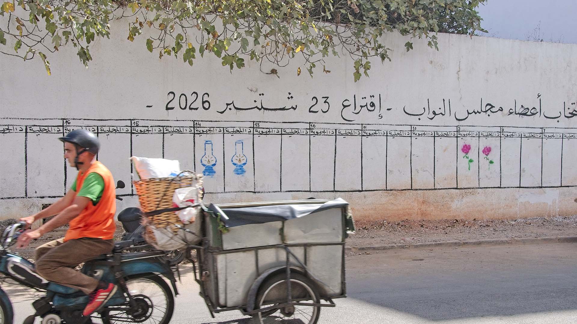 Un ciclomotor con un pequeño remolque pasa frente a unos paneles pintados en un muro sobre las elecciones legislativas en Marruecos de 2026 en una calle de Casablanca.