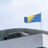 Bandera de Bosnia y Herzegovina ondeando sobre el edificio del Parlamento en Sarajevo, bajo un cielo nublado.