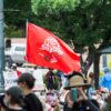 Una bandera roja con una rosa blanca y dos manos entrelazadas ondea sobre una multitud de manifestantes, algunos con pancartas contra el racismo, durante una protesta en Austin, Texas, el 31 de mayo de 2020.
