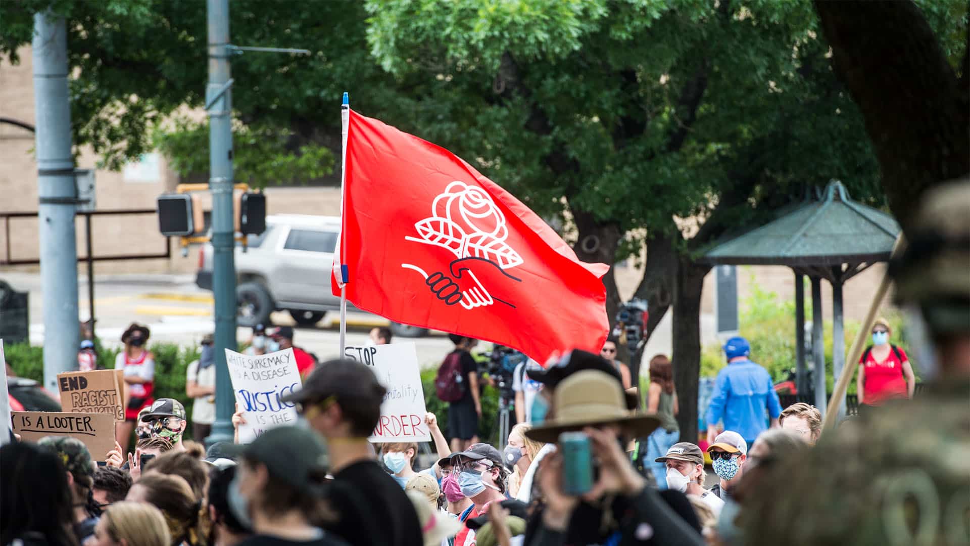 Una bandera roja con una rosa blanca y dos manos entrelazadas ondea sobre una multitud de manifestantes, algunos con pancartas contra el racismo, durante una protesta en Austin, Texas, el 31 de mayo de 2020.