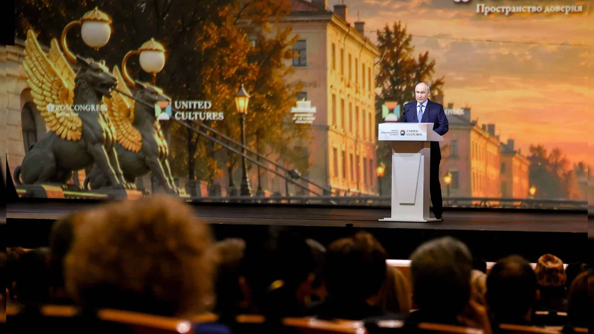 Vladímir Putin interviene desde un atril ante el público durante el XII Foro Internacional de las Culturas Unidas de San Petersburgo, con una gran pantalla de fondo con la imagen de la ciudad.