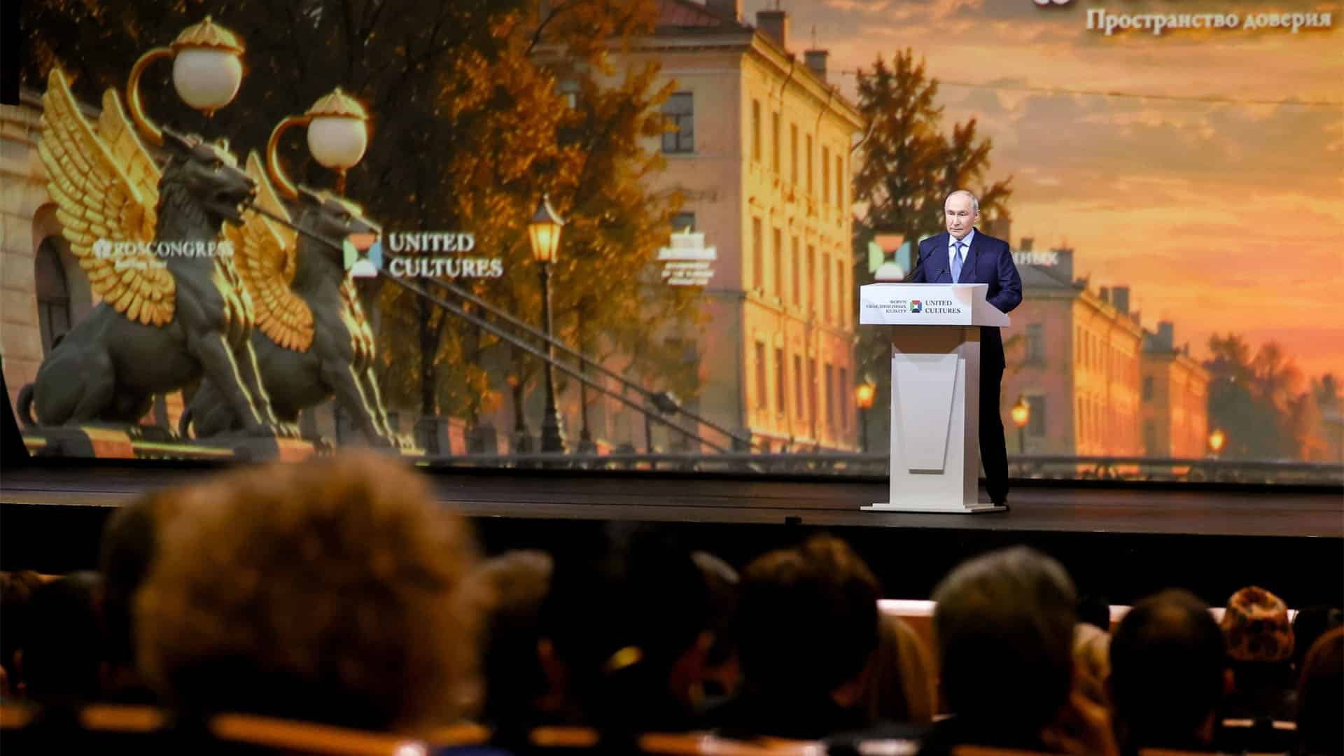 Vladímir Putin interviene desde un atril ante el público durante el XII Foro Internacional de las Culturas Unidas de San Petersburgo, con una gran pantalla de fondo que muestra una imagen de la ciudad.