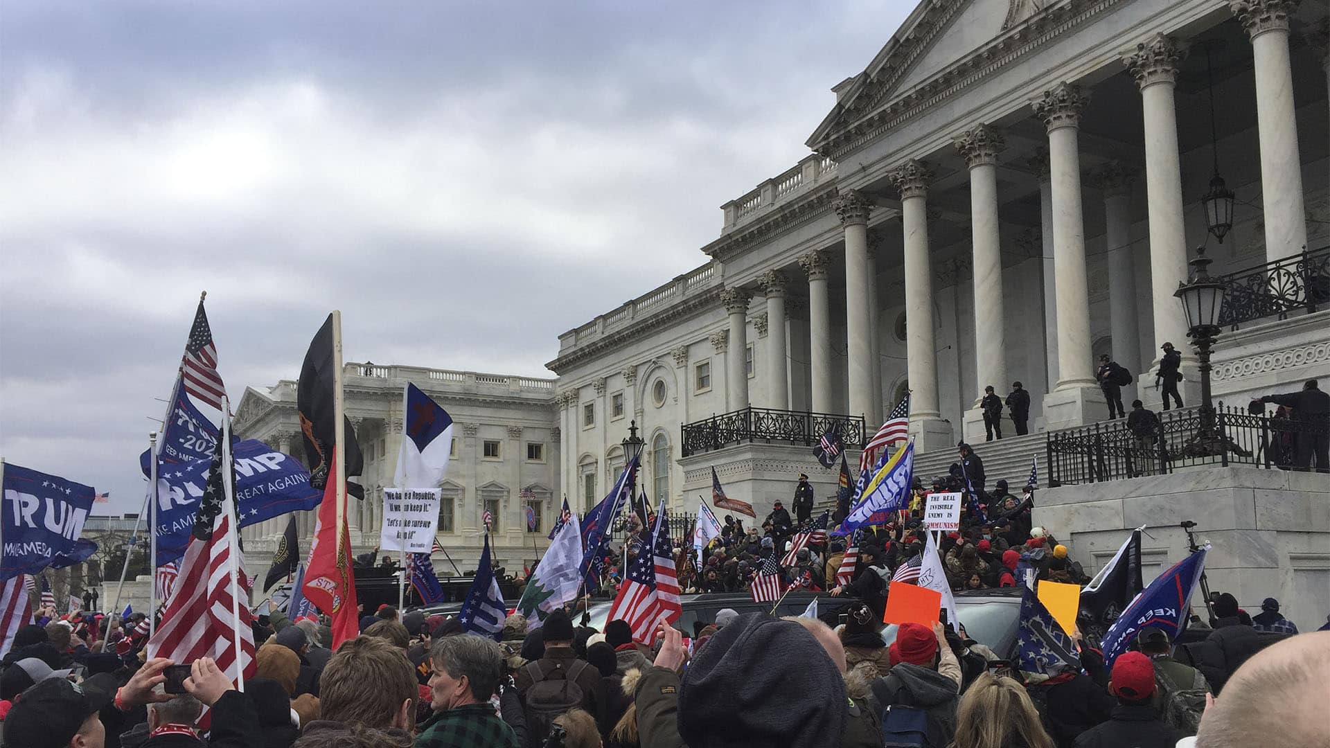 Multitud de manifestantes con banderas estadounidenses y pancartas de apoyo a Donald Trump se concentra frente al Capitolio de EEUU, mientras varias personas suben por las escalinatas del edificio durante el asalto del 6 de enero de 2021.