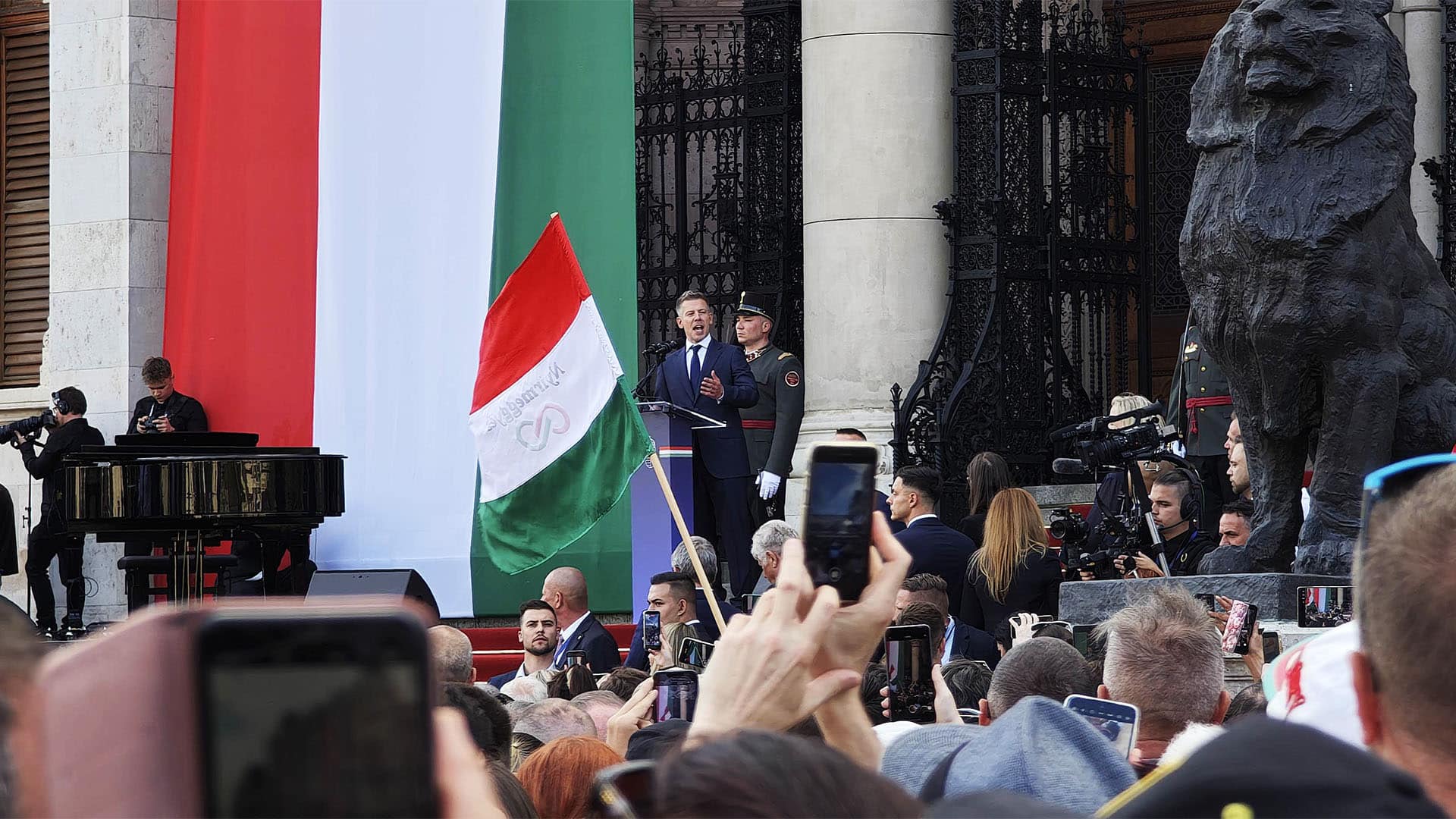 Péter Magyar pronuncia un discurso ante una multitud durante la constitución del Parlamento húngaro el 9 de mayo de 2026, con una gran bandera de Hungría de fondo y asistentes que graban el acto con sus teléfonos móviles.
