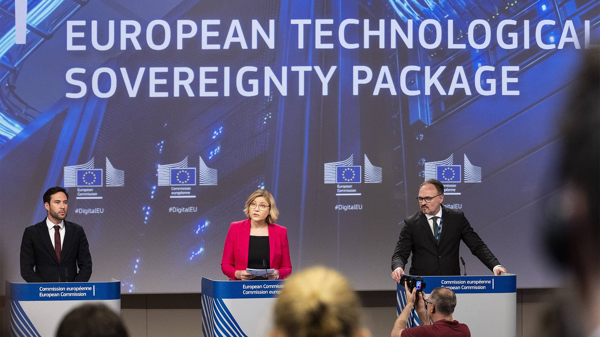Thomas Regnier, Henna Virkkunen and Dan Jørgensen, from left to right, stand behind three podiums during a European Commission press conference (03/06/2026). In the background, a screen displays the title “European Technological Sovereignty Package”.