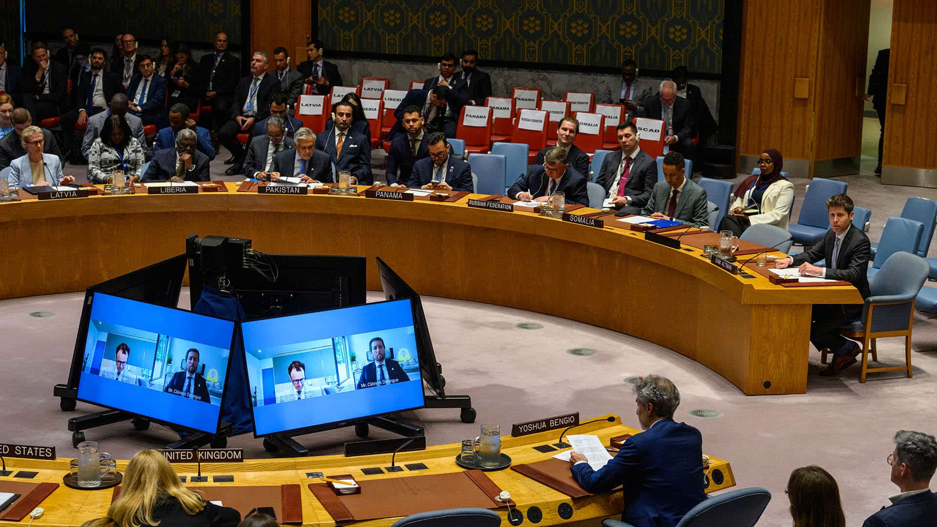 Sesión del Consejo de Seguridad de la ONU sobre inteligencia artificial y seguridad internacional, con representantes de distintos países sentados alrededor de una mesa circular, incluido Sam Altman (OpenAI) y las intervenciones de Dario Amodei (Anthropic) y Clem Delangue (Hugging Face) conectados por videoconferencia mostrados en las cinco pantallas centrales.