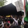 Multitud de manifestantes concentrados en Jantar Mantar, Nueva Delhi, durante una protesta estudiantil contra la filtración de los exámenes NEET UG, el 20 de julio de 2026. Los asistentes sostienen banderas de la India y pancartas reivindicativas, mientras algunos levantan los brazos frente a una carpa negra.