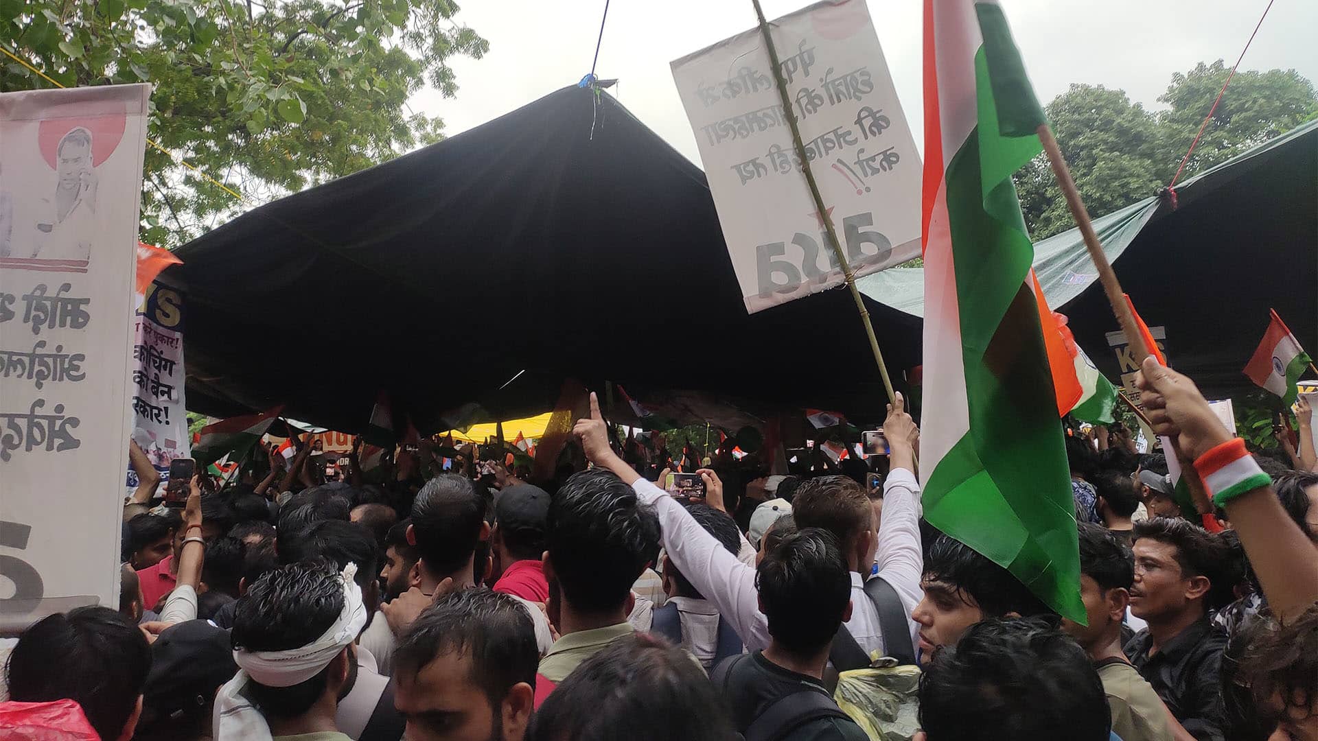 Multitud de manifestantes concentrados en Jantar Mantar, Nueva Delhi, durante una protesta estudiantil contra la filtración de los exámenes NEET UG, el 20 de julio de 2026. Los asistentes sostienen banderas de la India y pancartas reivindicativas, mientras algunos levantan los brazos frente a una carpa negra.