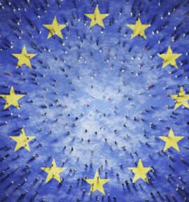 Aerial view of hundreds of people walking on a blue surface with twelve large yellow stars arranged in a circle, representing the European Union flag.