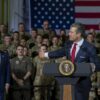 Pete Hegseth pronuncia unas palabras desde un atril con el sello presidencial de Estados Unidos ante el personal militar uniformado y una gran bandera estadounidense en el fondo.