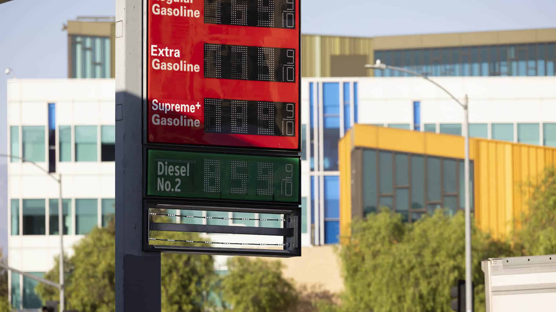 Un panel de precios en una gasolinera en Los Ángeles (EEUU) muestra los precios de la gasolina y diésel extremadamente altos. Al fondo edificios, dos farolas (una con) con semáforos y árboles en un día soleado.